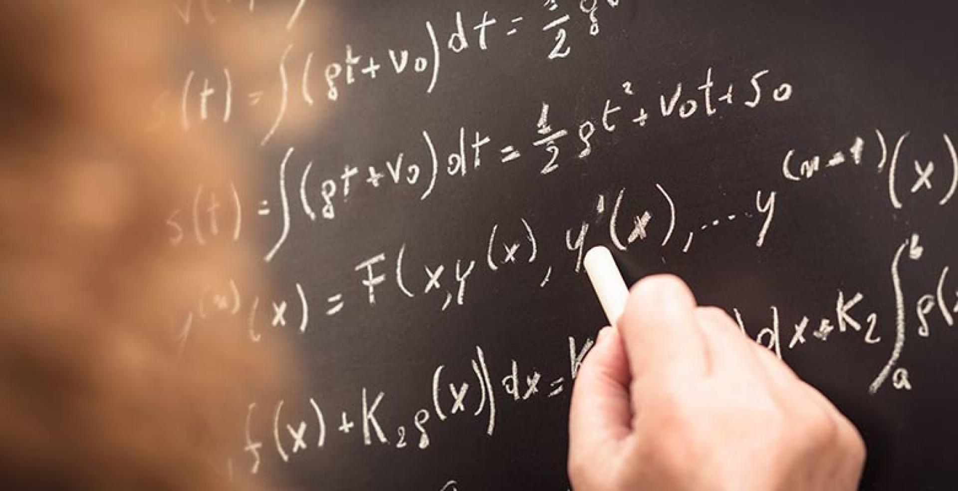 Person writing various formulas & equations on chalkboard